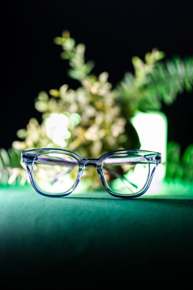 Transparente Brille vor einer grünen Beleuchtung und grünen Pflanzen.