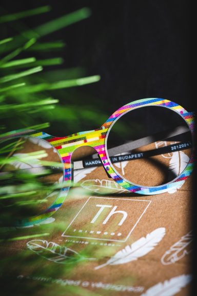 Bunte Brille liegt auf einem Notizbuch, umgeben von etwas Grün.