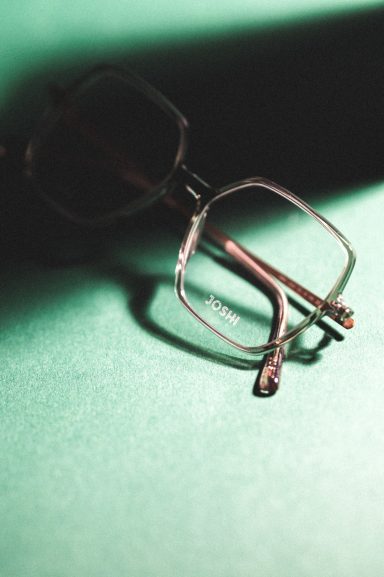 Auf einer grünen Oberfläche liegen eine Brille mit transparentem Gestell und einer Linse.